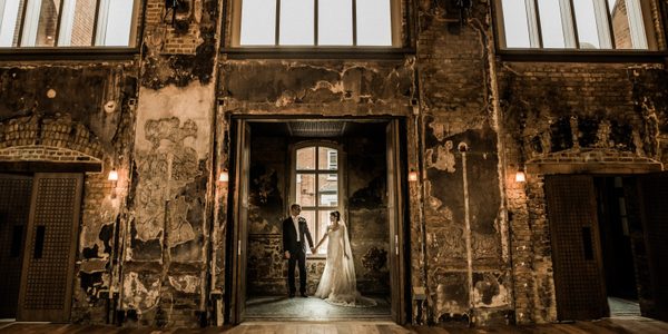 An image of a married couple stood holding hands in the door way into the Grand Hall.