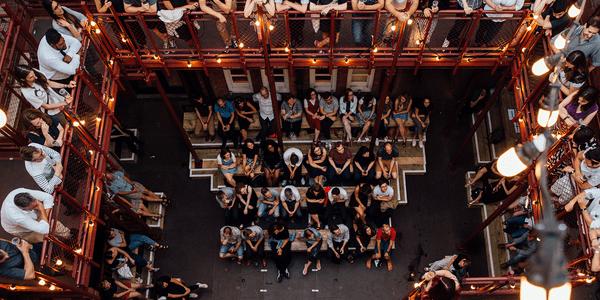 A bird's eye view of our courtyard, with three sides of audience. The standing gallery is above the seated audience, with lightbulbs draped over the balcony. The comedian looks up at the gallery.