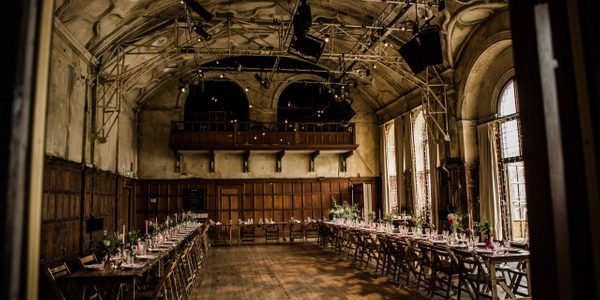 An image of the council chamber under preparation for a wedding. A lighting rig set up can be seen attached to the ceiling and long tables line the walls of the room with decorations.