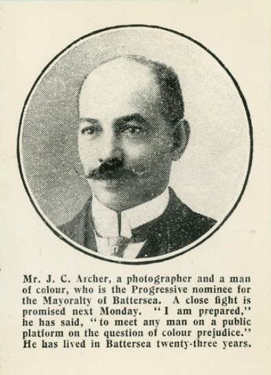 A black and white dappled photo in a cirlce of John Archer, ,a man with a moustache and a balding head. The caption reads 'Mr J C Archer, a photographer and a man of colour, who is the Progressive nominee for the Mayoralty of Battersea. A close fight is promised next Monday. 