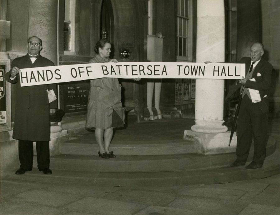 A black and white photograph of three people on the steps of our building, holding a banner reading 'Hands off Battersea Town Hall'.
