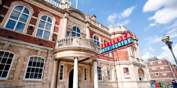 The front of our building, a Victorian town hall made from pale stone and red brick. The Battersea Arts Centre sign is extended from the entrance in red and blue with yellow lettering.