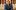 SeshieHenryAgency_Gallery_Image A young man wearing a blue jumper with a yellow butterfly on it smiles at the camera. He sits in front of a marble balcony, with books lined up on a ledge behind him