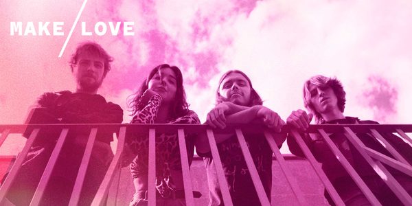 A pink filtered image of a band standing leant on a railing wearing black looking down at the camera.