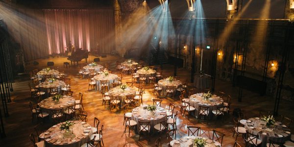 Tables set up for a wedding reception in the Grand Hall, with lots of round tables and a grand piano on the stage area.