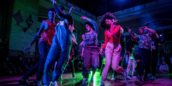 Image: When It Breaks It Burns. A group of young people dancing under multi-coloured lights. Photo by JMA Photography.