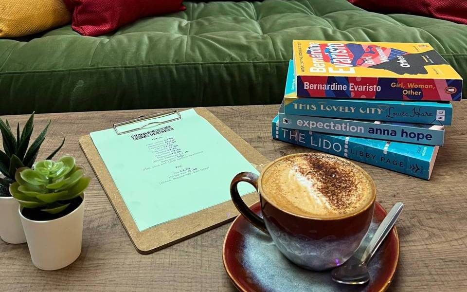 A coffee, a stack of books and a BAC drinks menu for the cafe