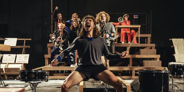 One-Song-c-Michiel-Devijver-2000x1000 A person wearing athletic clothing is screaming in a squat stance. There is a crowd of people standing behind him also shouting.
