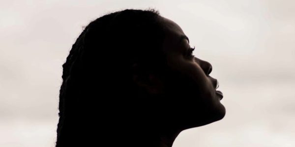 A Global Majority Woman in profile and partial silhouette looks up at the sky
