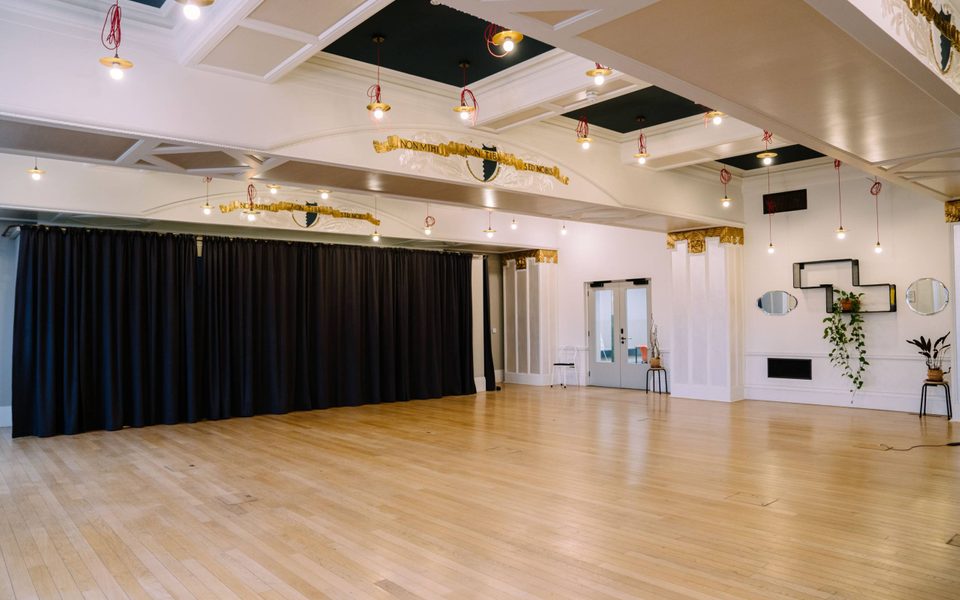 The Empty Lower Hall at Battersea Arts Centre. A black curtain runs along one wall and spotlights shine down on a wooden floor.