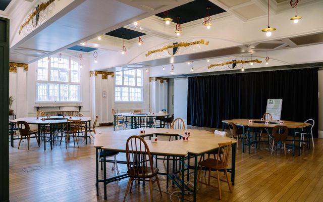 Battersea Arts Centre's Lower Hall set up for a meeting - several circular clusters of tables with chairs around their perimeters