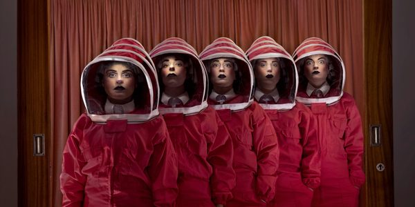 The Figs in Wigs company standing a line wearing dark orange boiler suits with bee-keeper style hoods.