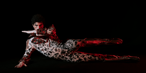 Natural Behaviour Credit Rocio Chacon 2000x1000 A male presenting person in a sparkling leopard costume lies on once side facing the camera, one leg and one arm raised.