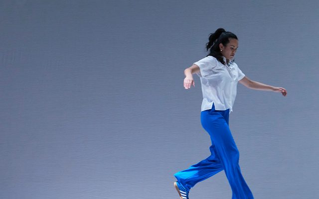 Rinse © Zan Wimberley A woman in blue trousers and a white shirt is mid-air as she steps off a blue plinth.