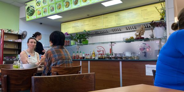 Interior of a cafe. There are people seated at a table facing each other engaged in conversation with the remains of their lunch on the table.