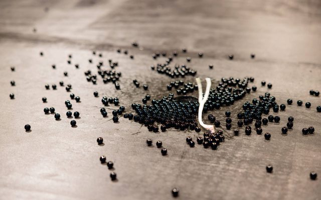 Black marble beads are scattered across a scratched black surface, there is a small string dispersing them.