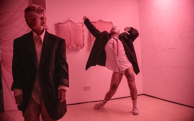 There is one person standing on the left walking away, another to the right dancing. They are both wearing black blazers and a white shirt with no trousers.