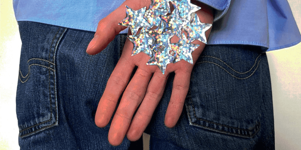 A hand is being held in front of a person wearing jeans and a blue shirt. Their palm is covered in silver stars.