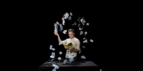 An image of a man reading a book whilst a confetti of playing cards falls around him.